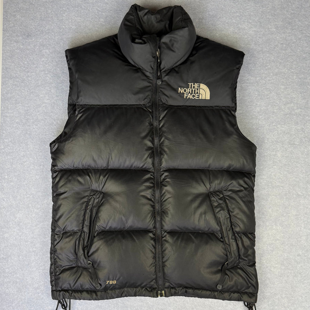 Black puffer vest with The North Face logo on a gray background