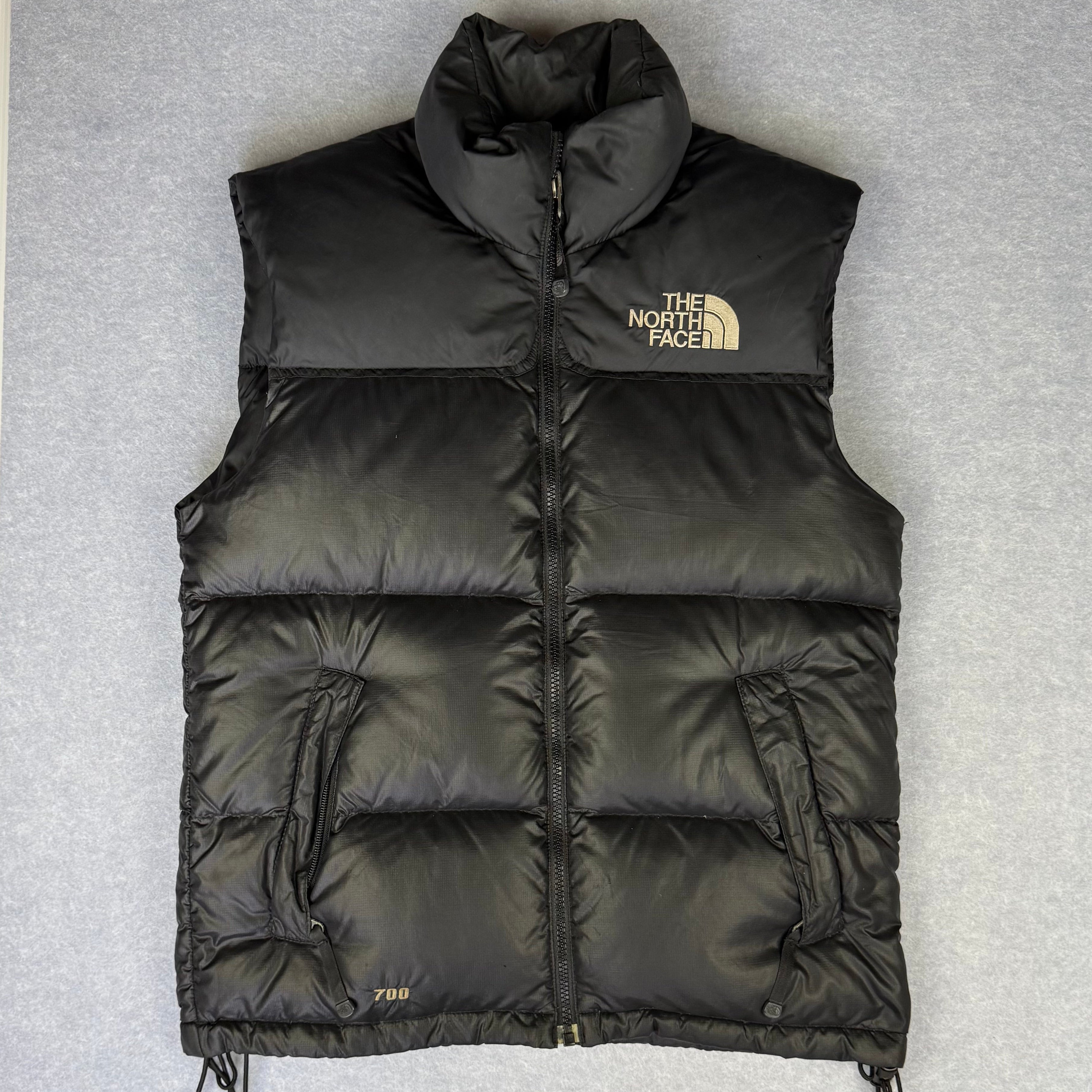 Black puffer vest with The North Face logo on a gray background