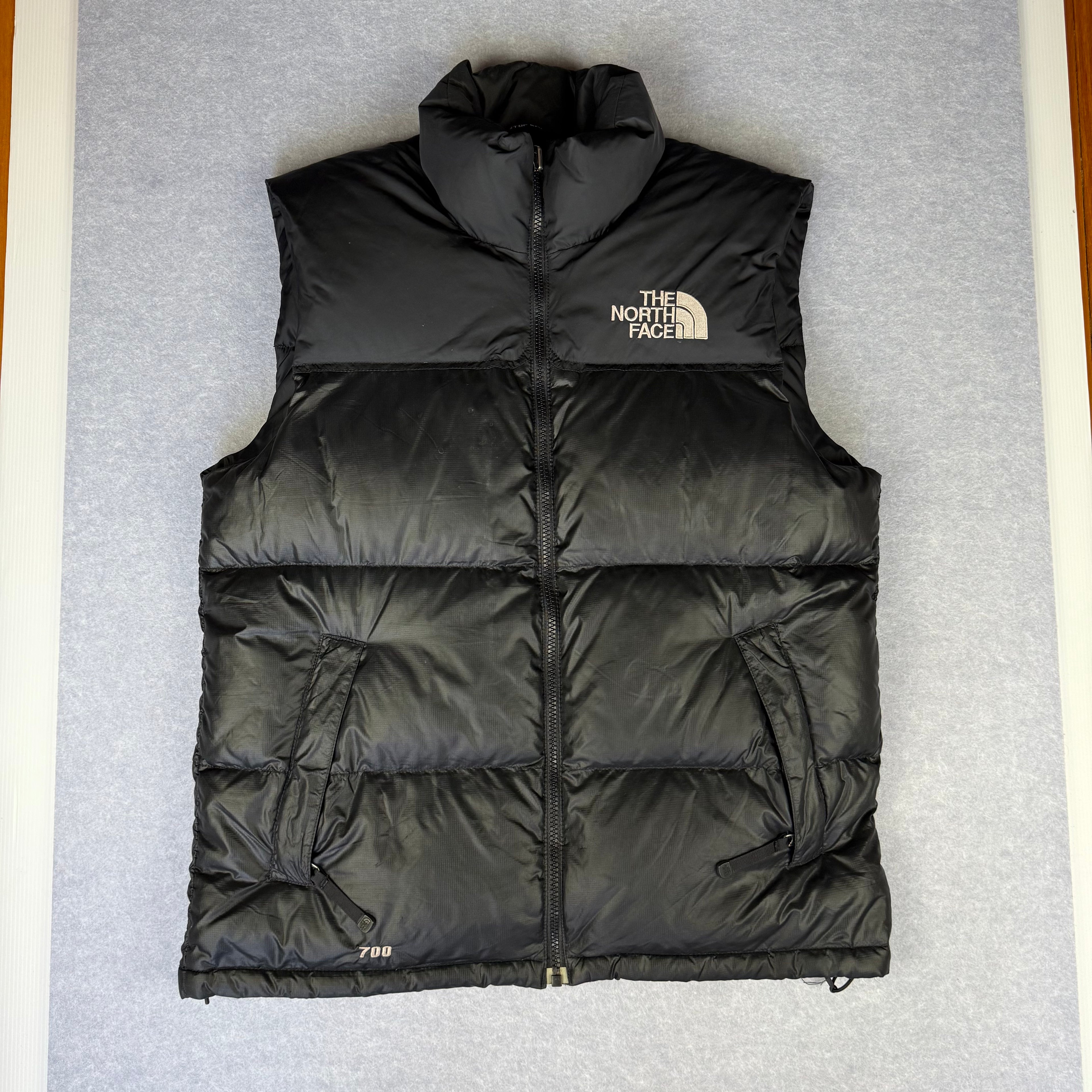 Black puffer vest with The North Face logo on a gray background
