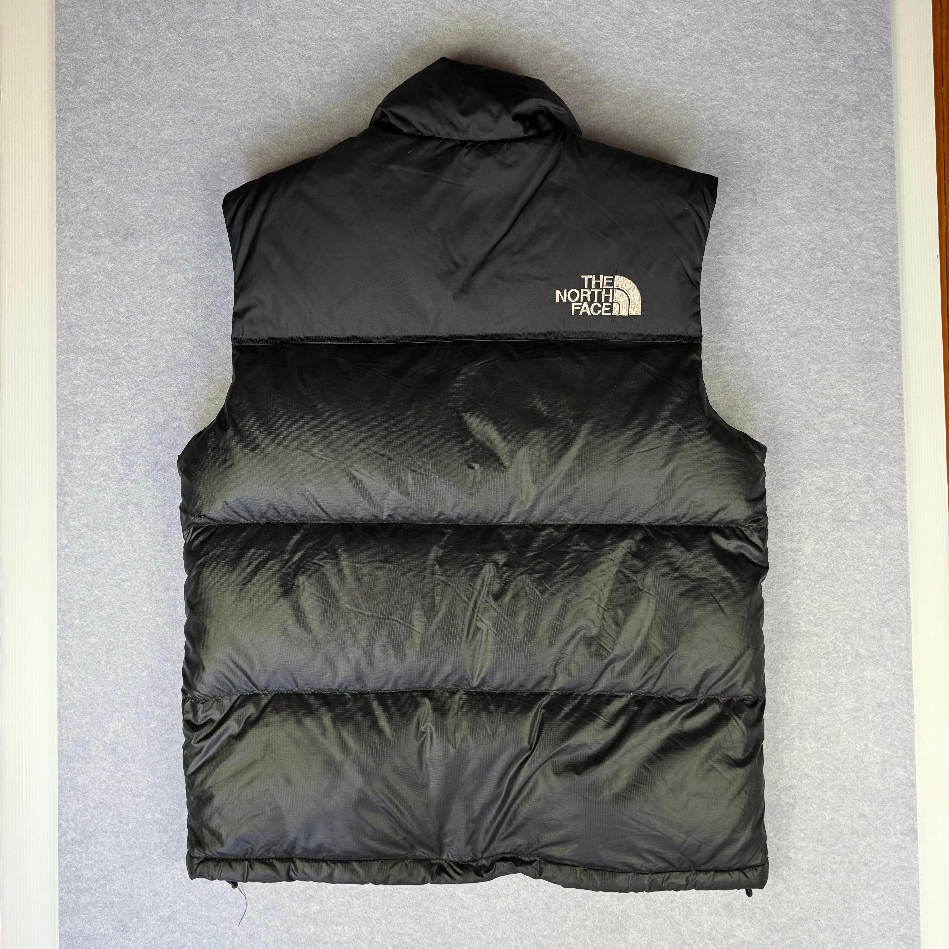 Rear of Black puffer vest with The North Face logo on a gray background